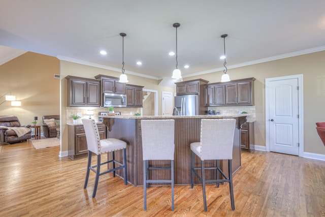 kitchen with appliances with stainless steel finishes, a breakfast bar, light wood finished floors, and dark brown cabinets