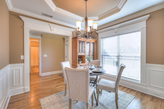 dining area with light wood finished floors, visible vents, a wainscoted wall, a tray ceiling, and a chandelier