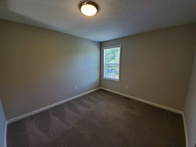 spare room featuring dark colored carpet, visible vents, and baseboards