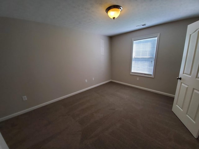 unfurnished room featuring visible vents, dark carpet, a textured ceiling, and baseboards