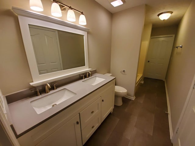 full bathroom featuring toilet, double vanity, baseboards, and a sink