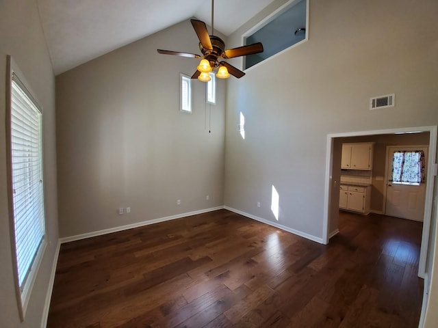 empty room featuring baseboards, visible vents, dark wood finished floors, ceiling fan, and vaulted ceiling