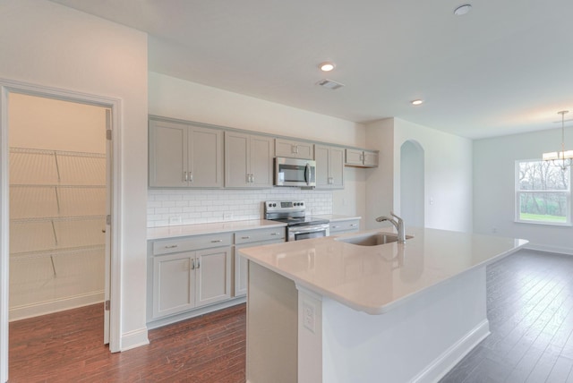 kitchen with stainless steel appliances, gray cabinets, a sink, and dark wood finished floors