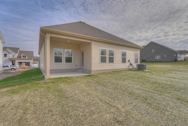 rear view of house featuring a yard, roof with shingles, central AC unit, and a patio