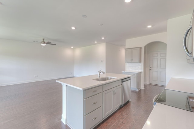 kitchen featuring arched walkways, dark wood finished floors, a center island with sink, a sink, and dishwasher