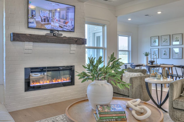 living area with crown molding, recessed lighting, visible vents, a brick fireplace, and wood finished floors