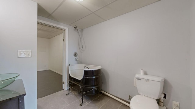 full bath featuring a drop ceiling, toilet, a tub to relax in, tile patterned floors, and vanity