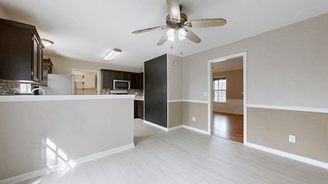 kitchen with light wood-style flooring, freestanding refrigerator, decorative backsplash, dark brown cabinetry, and stainless steel microwave