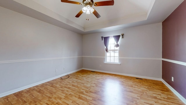 spare room with light wood-type flooring, visible vents, a ceiling fan, baseboards, and a raised ceiling