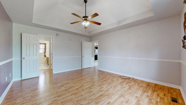 empty room featuring visible vents, light wood-style flooring, baseboards, and a tray ceiling