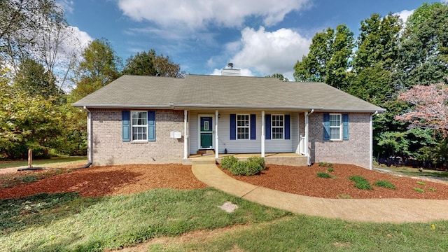 ranch-style home featuring brick siding, a porch, a chimney, and a front yard