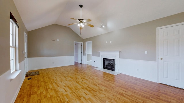 unfurnished living room featuring a wainscoted wall, light wood-style flooring, a ceiling fan, a high end fireplace, and lofted ceiling