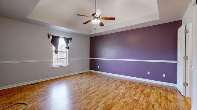 empty room featuring visible vents, light wood-style flooring, a raised ceiling, and baseboards