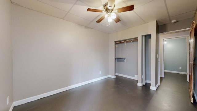 unfurnished bedroom with a closet, finished concrete floors, a paneled ceiling, and baseboards