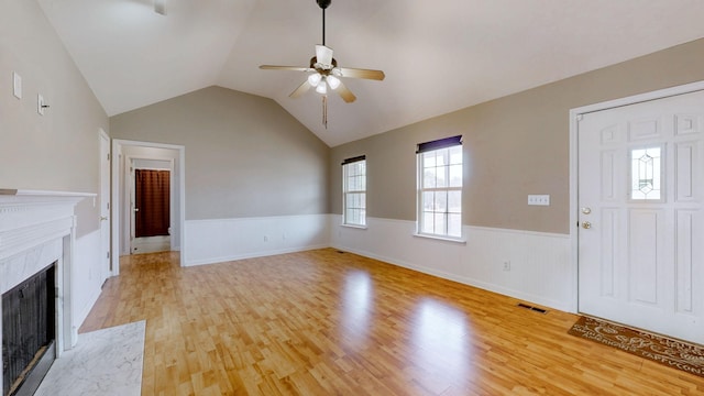 unfurnished living room featuring visible vents, a wainscoted wall, light wood finished floors, lofted ceiling, and a tile fireplace