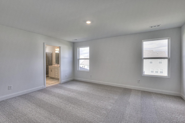 unfurnished bedroom with ensuite bathroom, recessed lighting, light colored carpet, visible vents, and baseboards