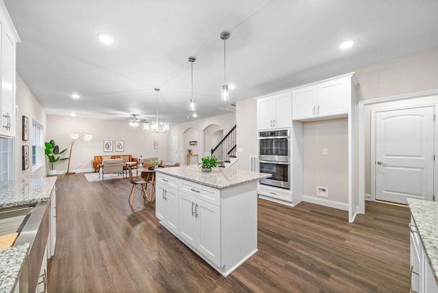 kitchen with dark wood-type flooring, open floor plan, arched walkways, stainless steel double oven, and white cabinetry