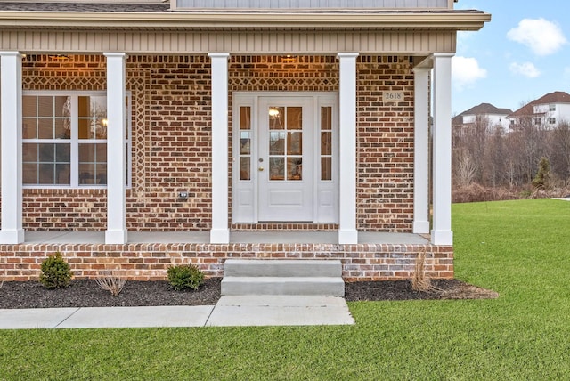 doorway to property with brick siding, covered porch, and a yard