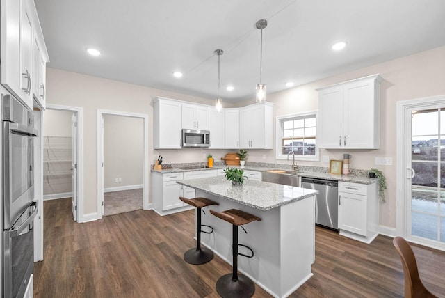 kitchen featuring a healthy amount of sunlight, a sink, stainless steel appliances, white cabinetry, and a center island