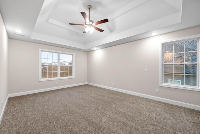 spare room with carpet flooring, visible vents, a raised ceiling, and baseboards