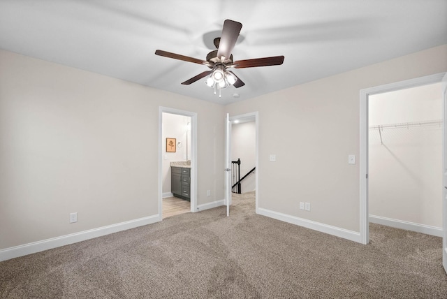 unfurnished bedroom featuring a walk in closet, baseboards, a closet, and light carpet