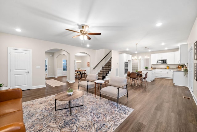 living area featuring ceiling fan with notable chandelier, recessed lighting, arched walkways, baseboards, and dark wood-style flooring