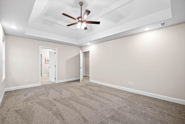 unfurnished bedroom with baseboards, visible vents, a raised ceiling, and light carpet