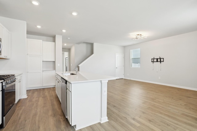 kitchen featuring stainless steel appliances, recessed lighting, light wood-style floors, a sink, and an island with sink