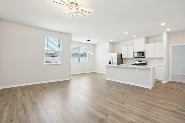 kitchen featuring stainless steel appliances, open floor plan, a center island with sink, and light wood-style flooring