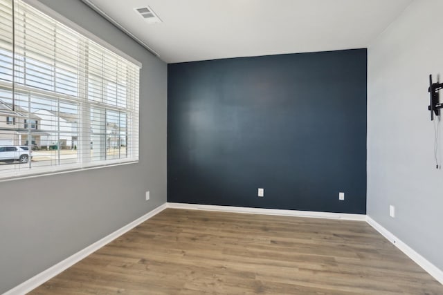 empty room featuring visible vents, an accent wall, baseboards, and wood finished floors