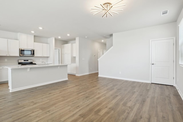 kitchen with light wood finished floors, appliances with stainless steel finishes, open floor plan, a kitchen island with sink, and white cabinets