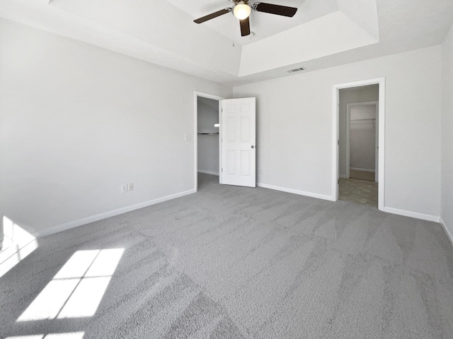 unfurnished bedroom with visible vents, a tray ceiling, baseboards, and carpet flooring