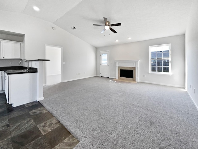 unfurnished living room with a ceiling fan, lofted ceiling, dark carpet, a sink, and a high end fireplace