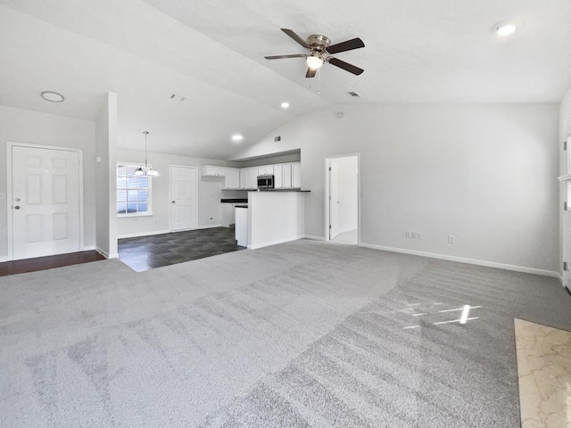 unfurnished living room featuring ceiling fan with notable chandelier, dark colored carpet, vaulted ceiling, and baseboards