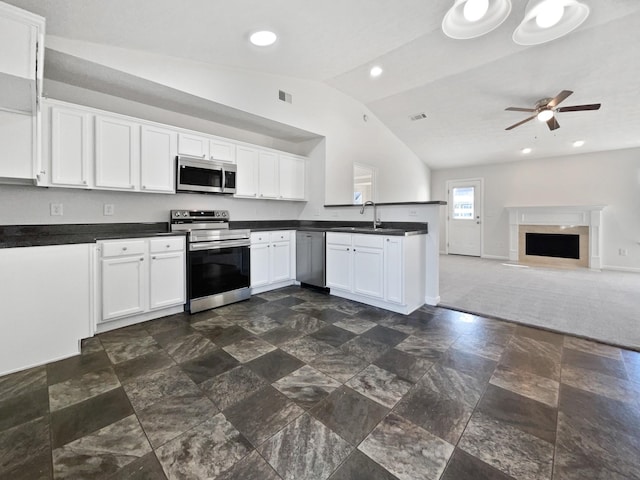 kitchen featuring dark countertops, a premium fireplace, vaulted ceiling, stainless steel appliances, and white cabinetry