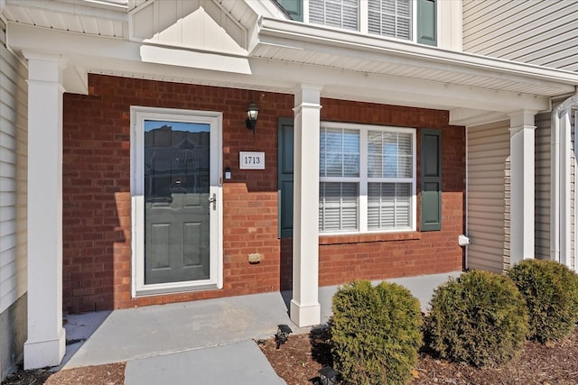 entrance to property featuring covered porch, board and batten siding, and brick siding