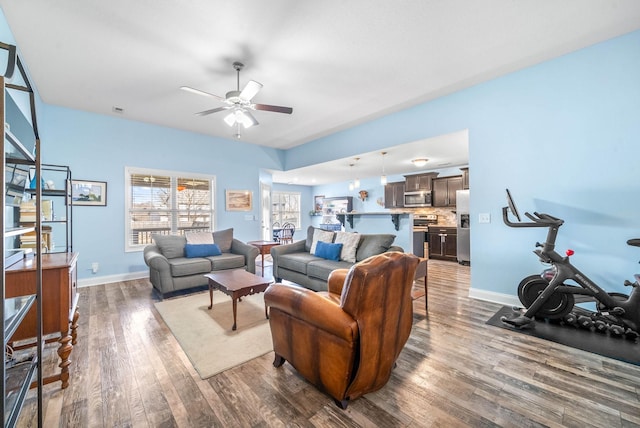 living area featuring dark wood-type flooring, ceiling fan, and baseboards