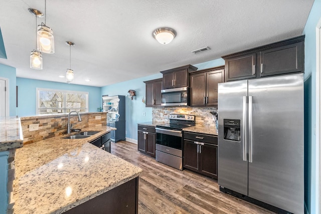 kitchen featuring dark brown cabinetry, stainless steel appliances, a sink, visible vents, and backsplash