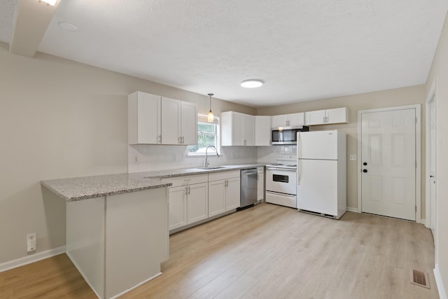 kitchen featuring appliances with stainless steel finishes, a peninsula, light stone countertops, light wood-type flooring, and white cabinetry