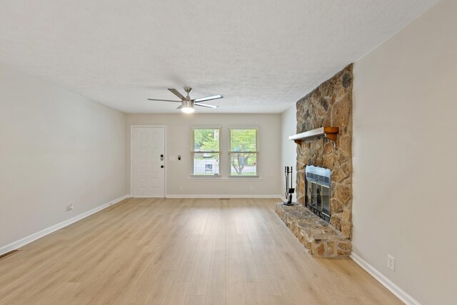 unfurnished living room featuring a textured ceiling, a fireplace, a ceiling fan, baseboards, and light wood finished floors