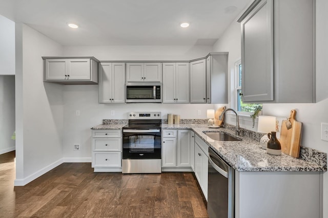 kitchen with appliances with stainless steel finishes, dark wood-style flooring, light stone countertops, gray cabinetry, and a sink