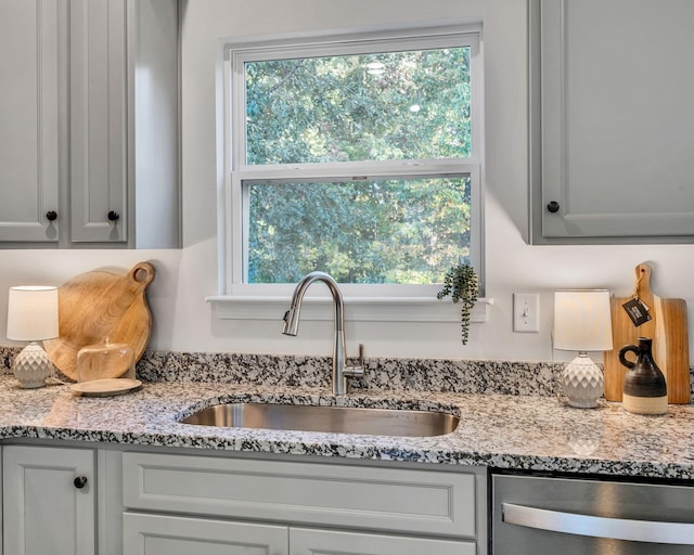 kitchen featuring stainless steel dishwasher, plenty of natural light, a sink, and light stone counters