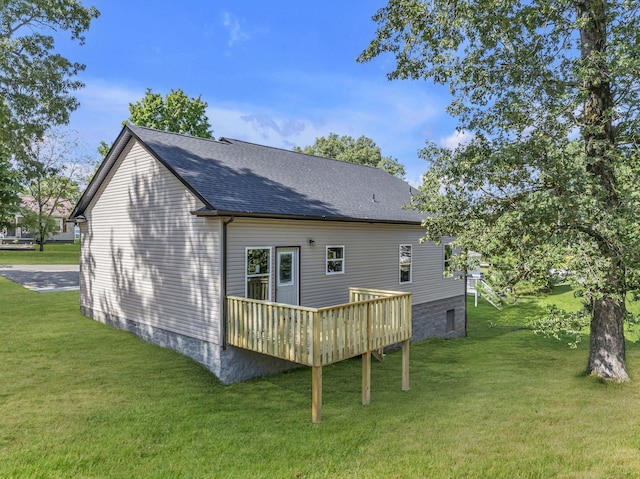 rear view of property with a shingled roof, a lawn, and a wooden deck