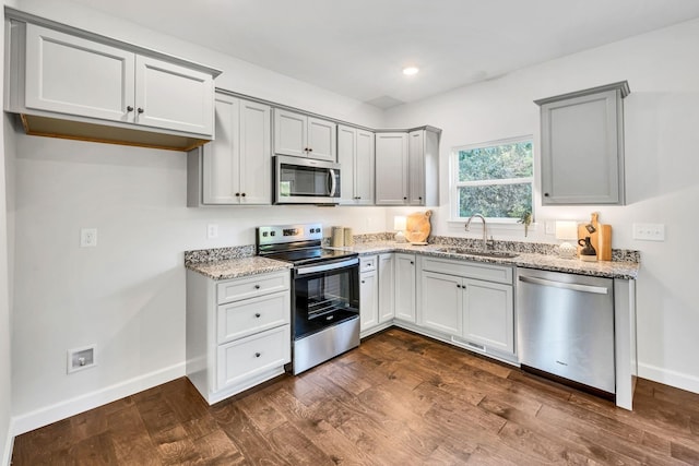 kitchen featuring light stone counters, dark wood-style flooring, appliances with stainless steel finishes, a sink, and baseboards