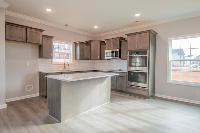 kitchen featuring baseboards, decorative backsplash, ornamental molding, stainless steel appliances, and a sink