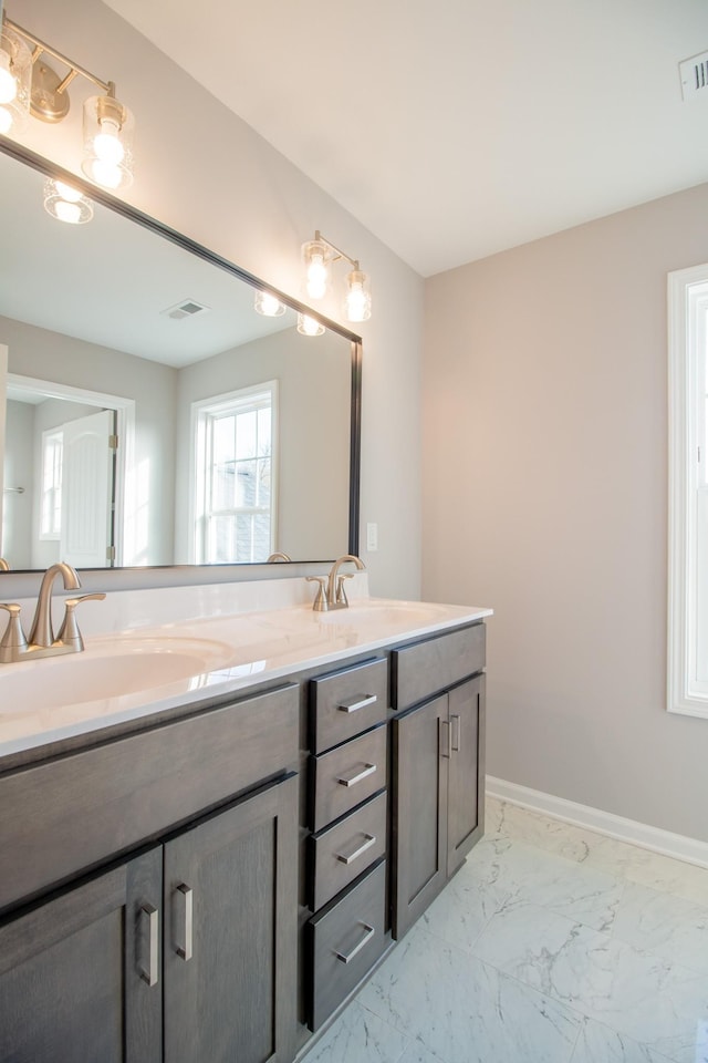 full bathroom with marble finish floor, double vanity, a sink, and baseboards