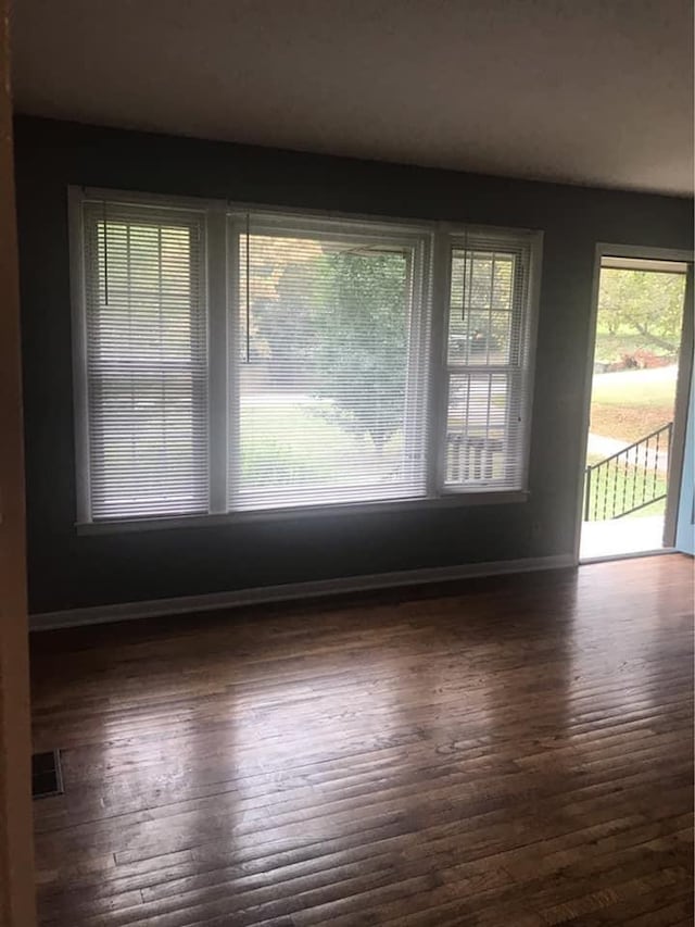 spare room featuring visible vents, plenty of natural light, baseboards, and wood finished floors