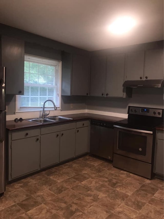 kitchen with dark countertops, under cabinet range hood, appliances with stainless steel finishes, and a sink