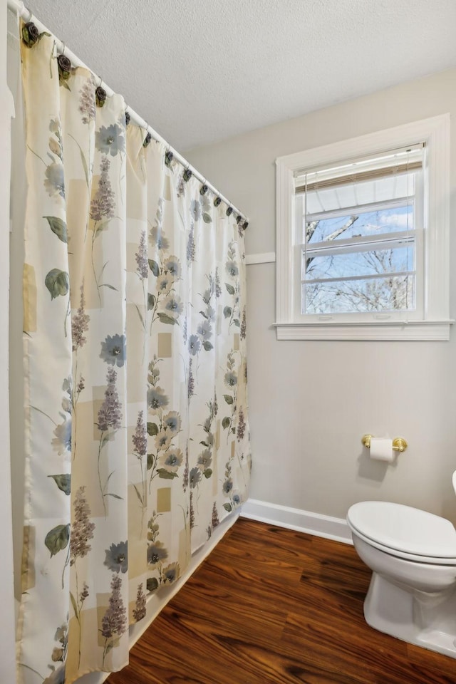 bathroom featuring baseboards, toilet, wood finished floors, curtained shower, and a textured ceiling