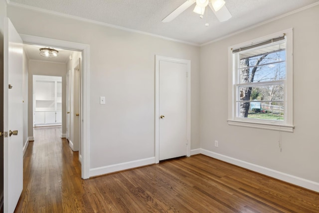 unfurnished bedroom featuring dark wood-style floors, crown molding, a textured ceiling, and baseboards